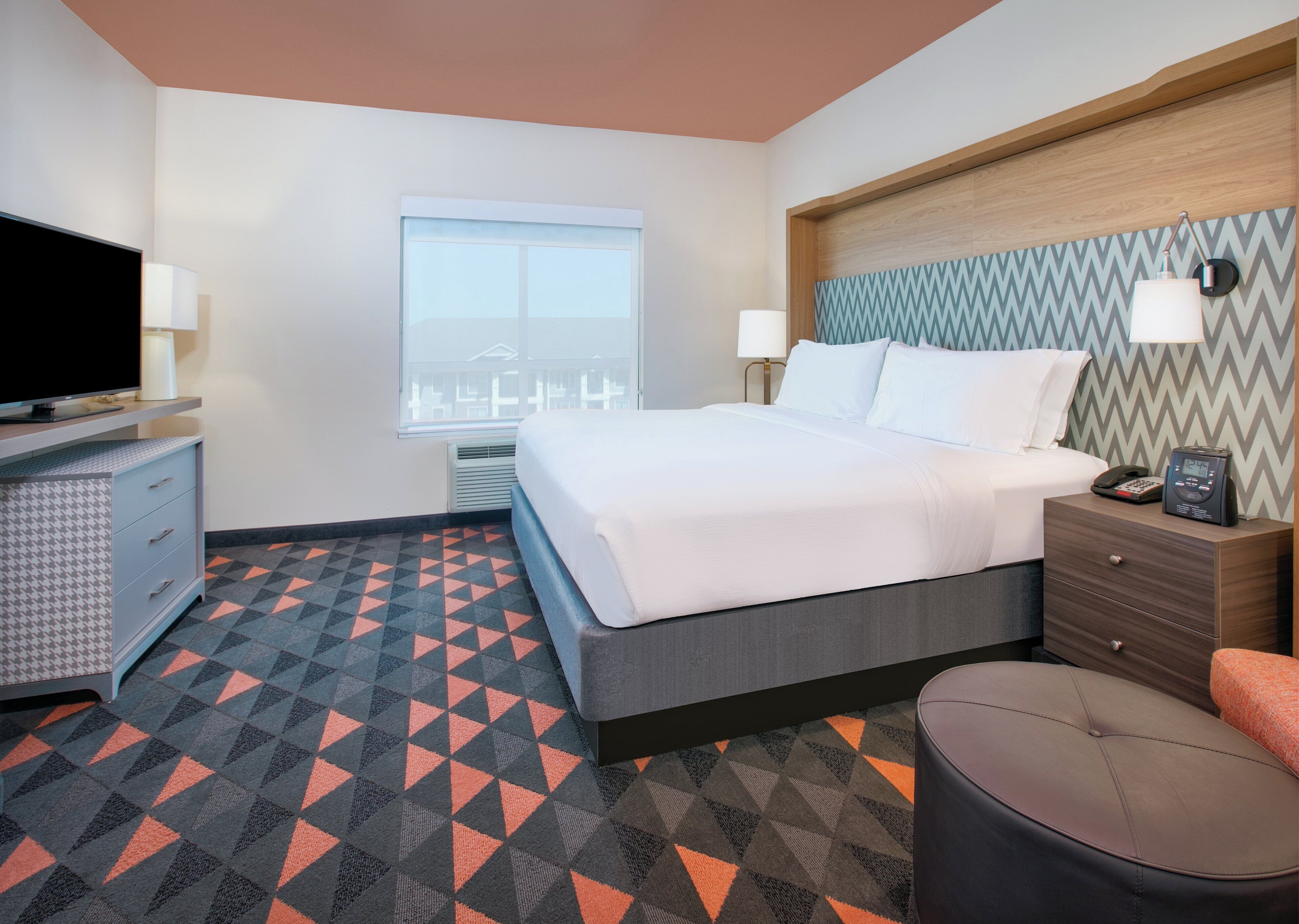 A hotel room with a bed, bedside table, TV, and a patterned floor.