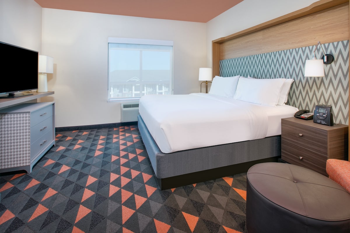 A hotel room with a bed, bedside table, TV, and a patterned floor.