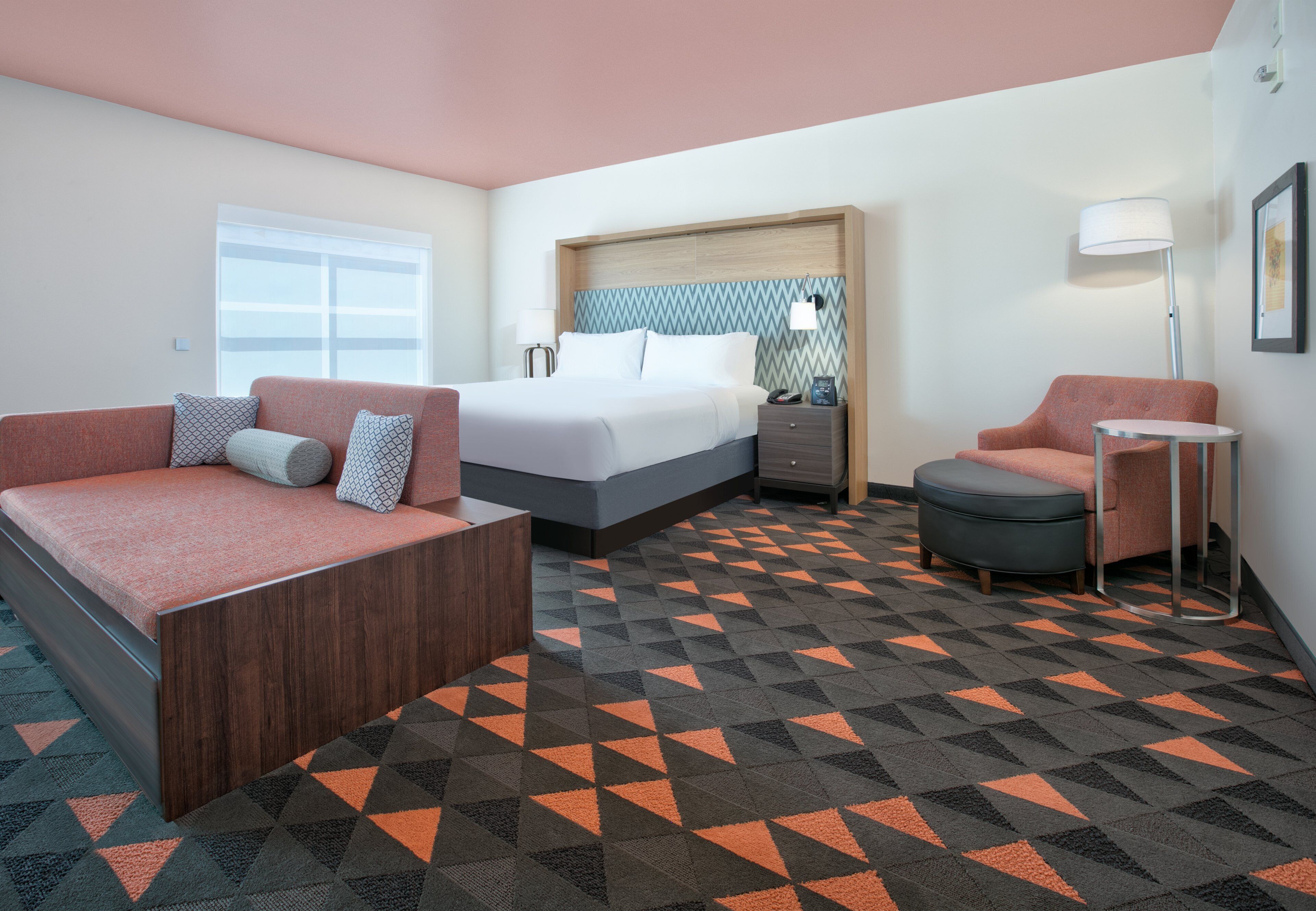 A hotel room with a bed, a sofa, a chair, a desk, and a lamp.