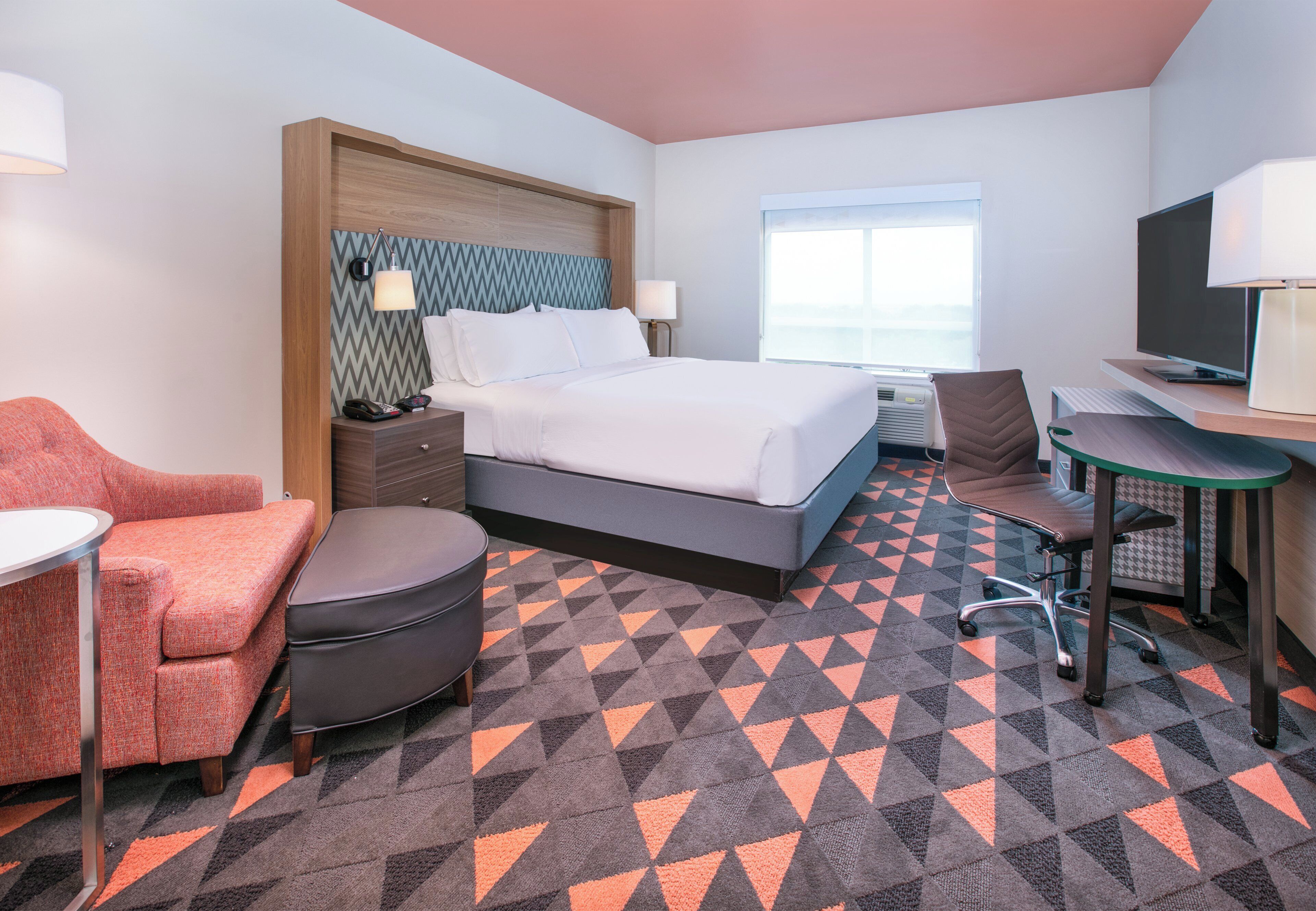 A hotel room with a bed, a desk, a chair, a sofa, and a TV.