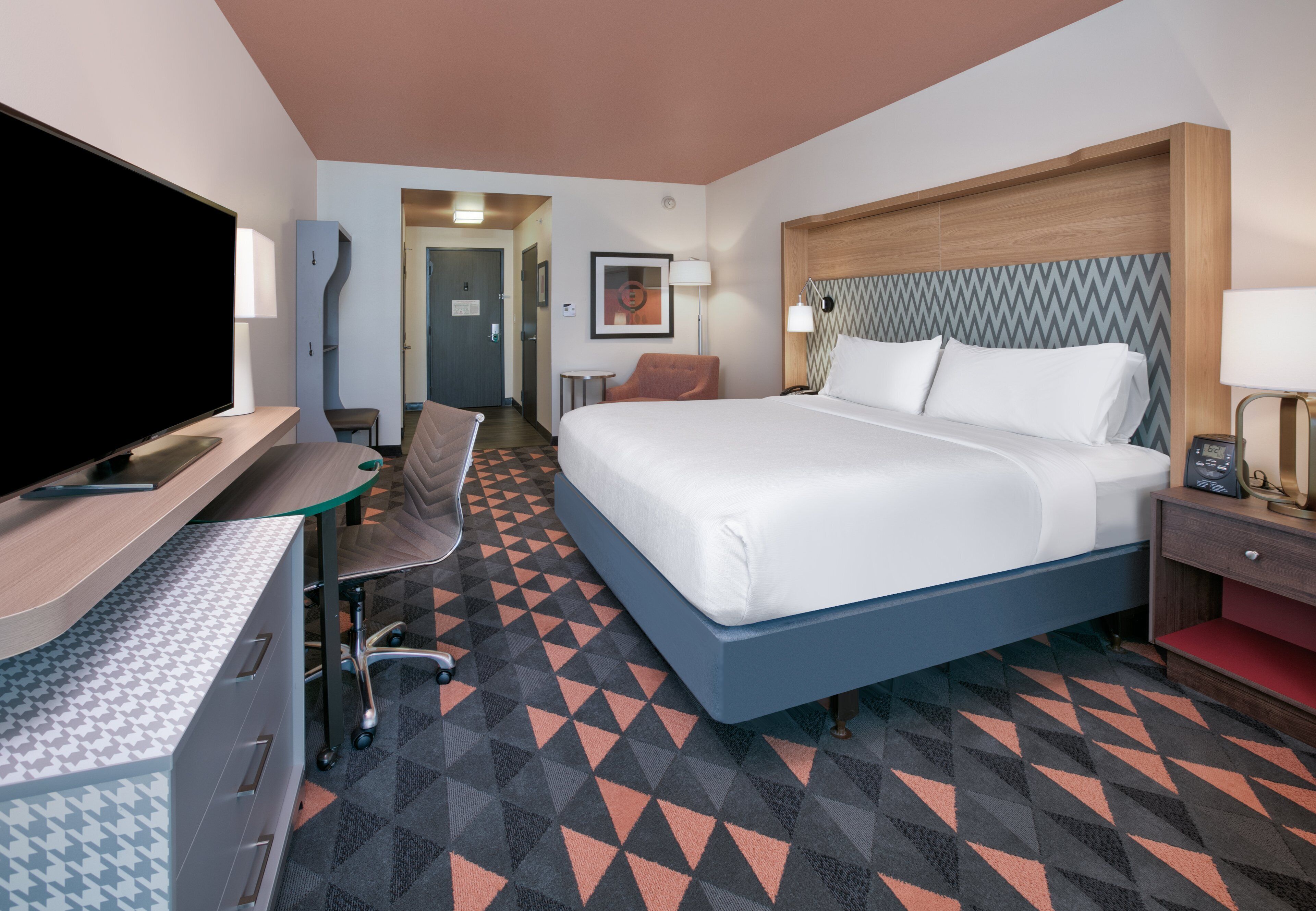 Een hotelkamer met een groot bed, een bureau met een flatscreen televisie, een stoel en een klein tafeltje.