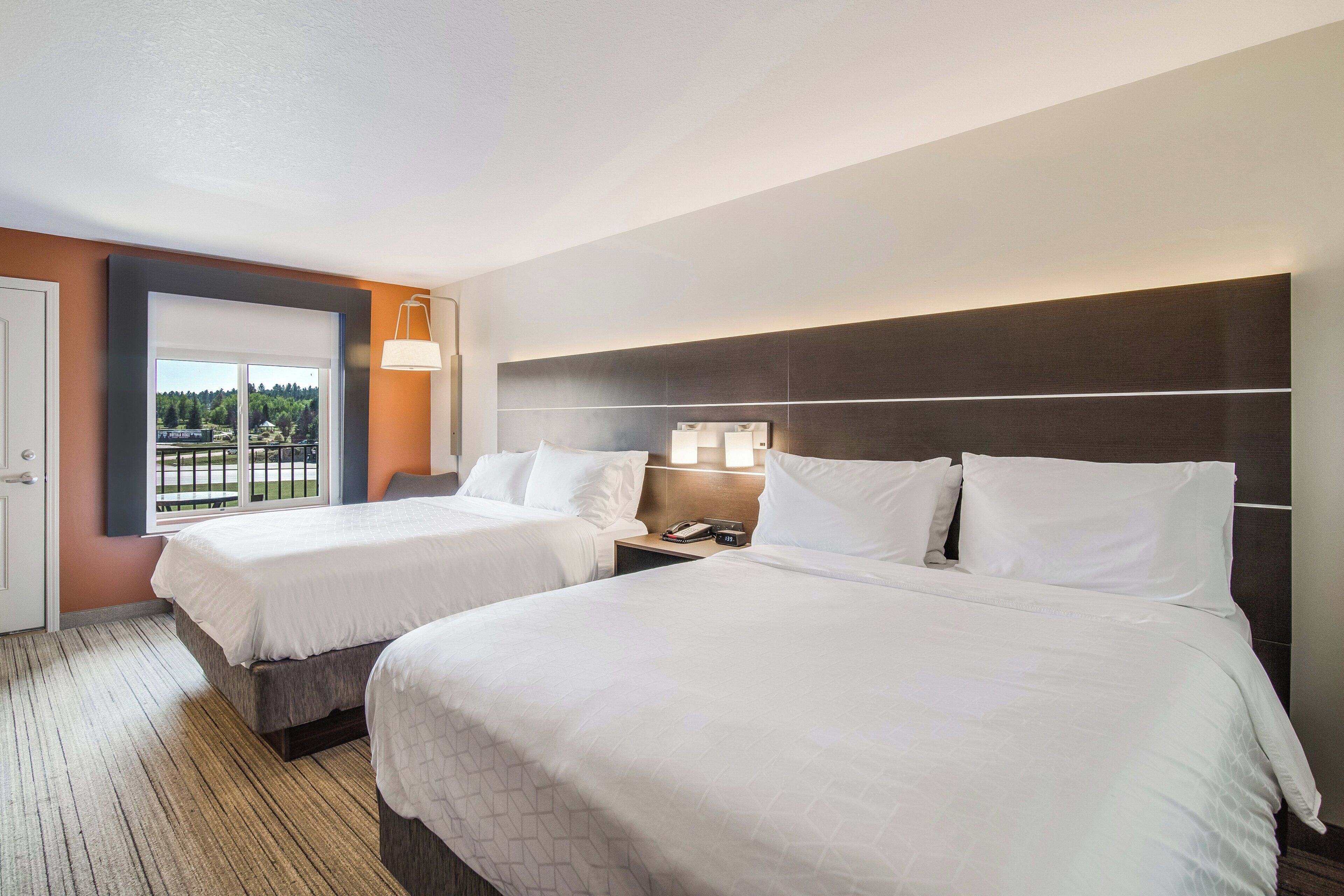 A hotel room with two beds, a large window with a view, and a nightstand with a lamp.