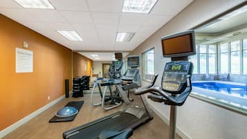 Un centre de remise en forme équipé de tapis de course, de vélos elliptiques et d’une piscine visible à travers la fenêtre.