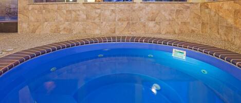 Piscina circular com interior azul, rodeada por uma moldura de tijolos, e um painel de azulejos com janelas acima.
