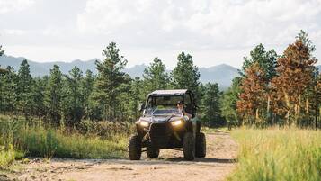 A vehicle on a dirt path surrounded by trees and mountains.