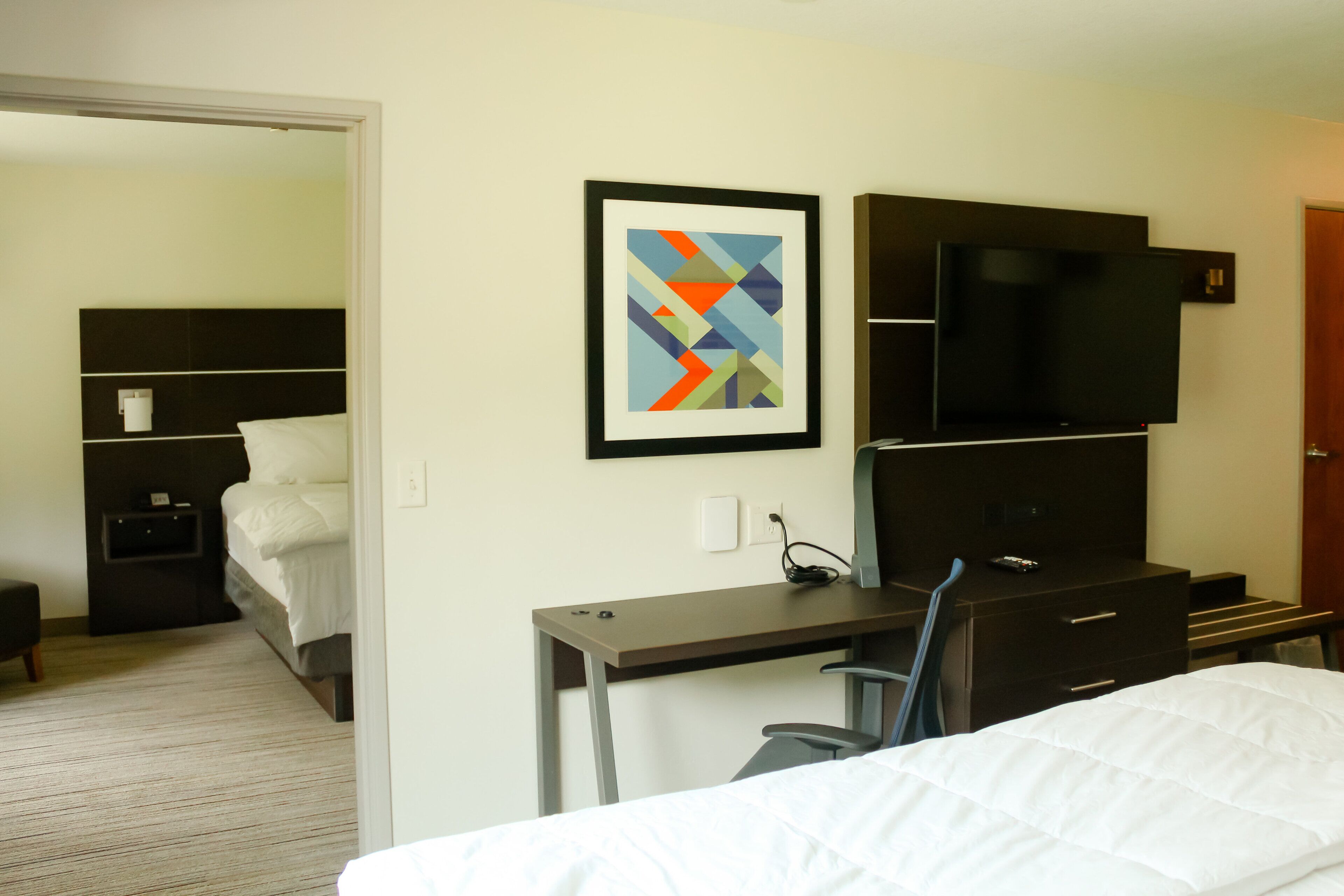 Una habitación de hotel con cama, escritorio, silla, televisión y un cuadro en la pared.