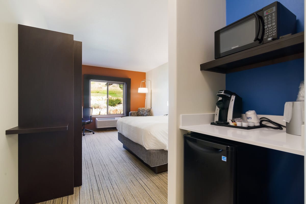 A hotel room with a bed, a desk with a microwave, a coffee maker, and a refrigerator.