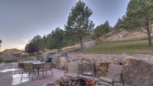 An outdoor patio with a stone fire pit, seating, and a view of a grassy hillside. - Holiday Inn Express Hotel & Suites Custer by IHG (Custer)