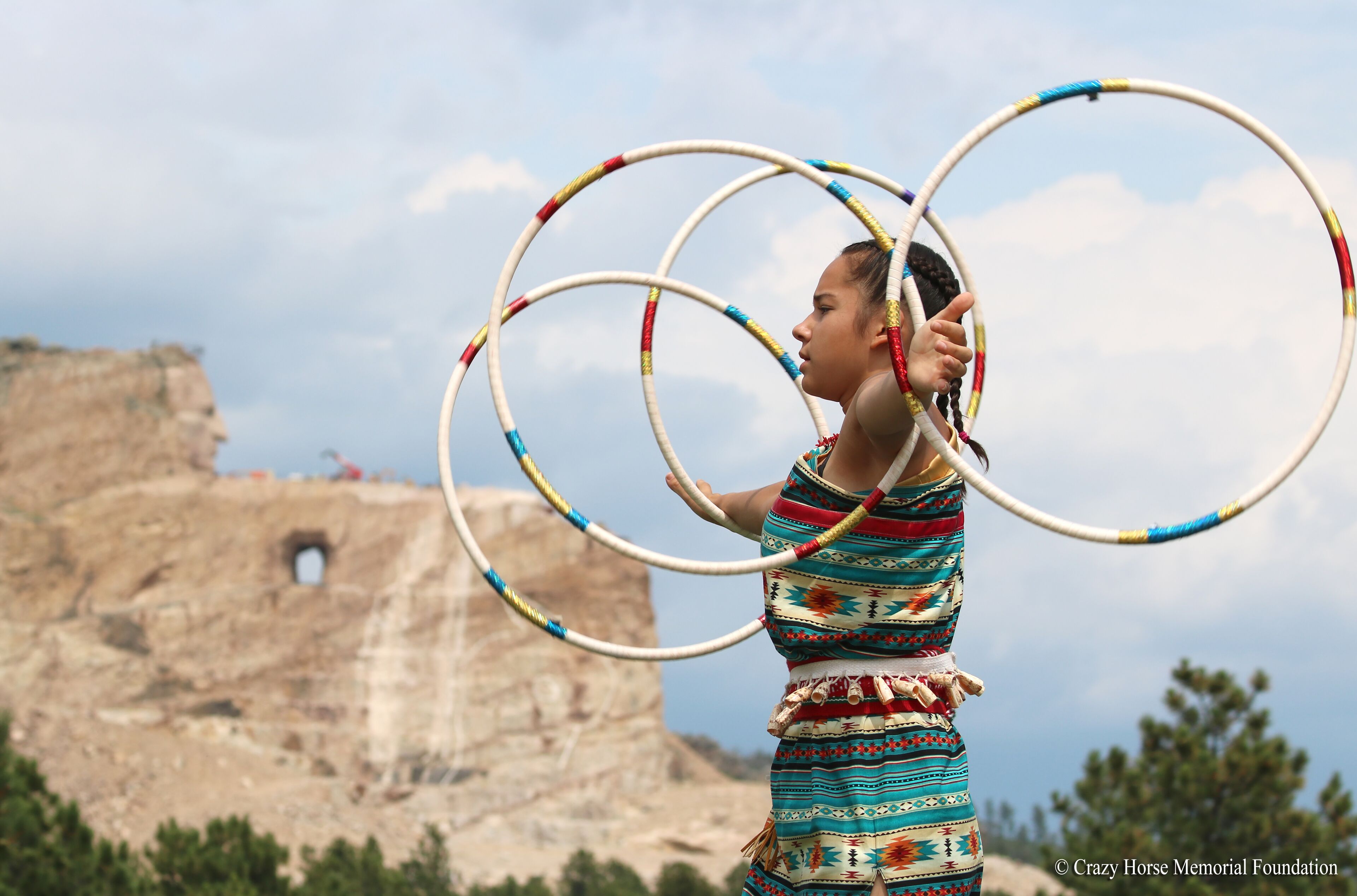 A person performing with hula hoops in an outdoor setting with a rocky cliff in the background.