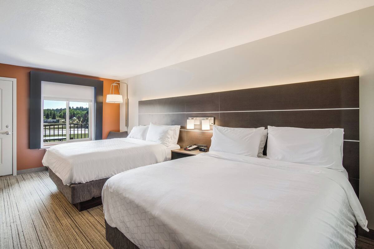 A hotel room with two beds, a large window with a view, and a nightstand with a lamp.