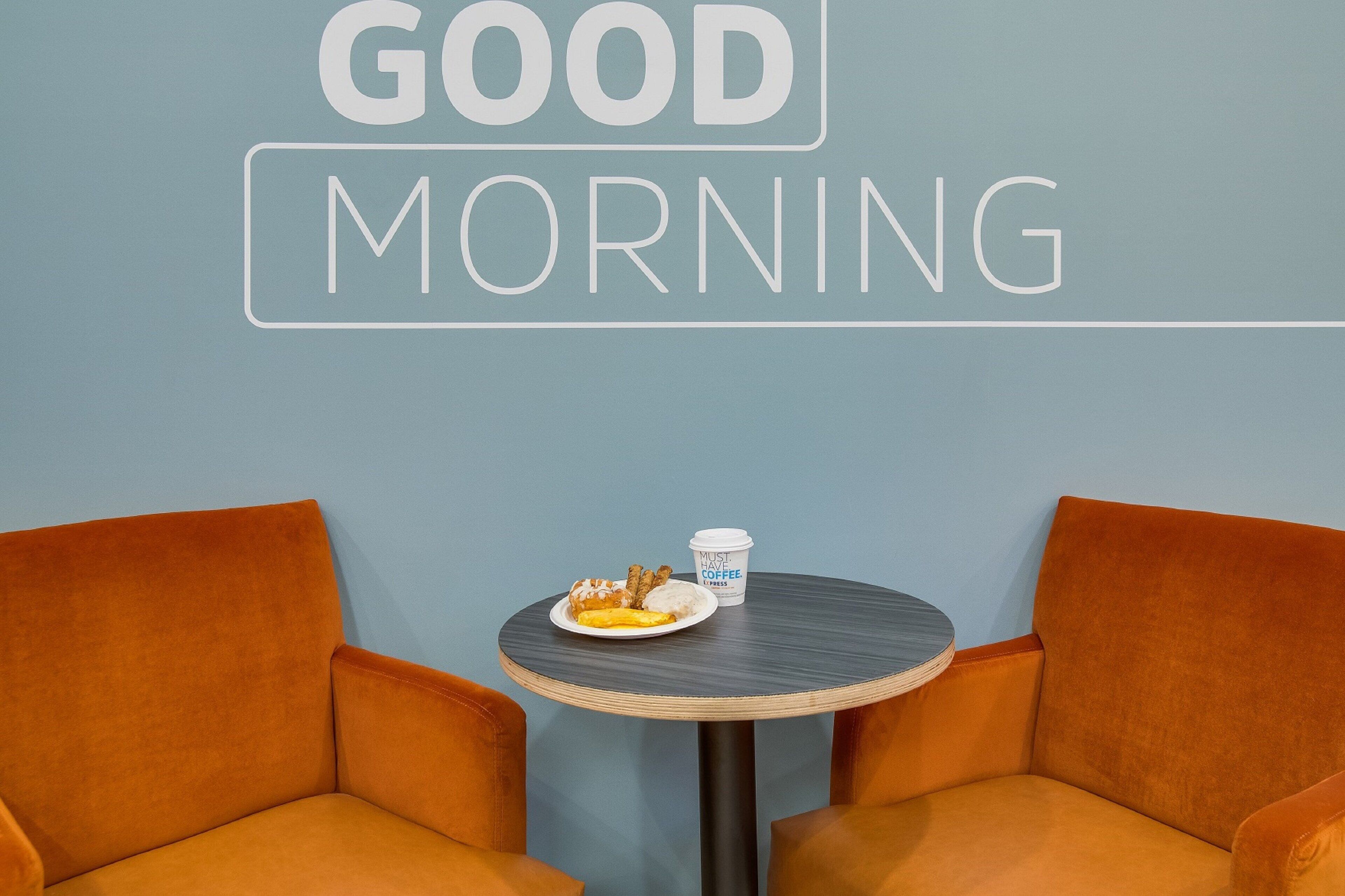 A room with a blue wall, a round table with a coffee cup and a plate of food, and two orange chairs.