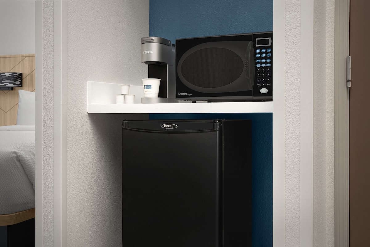 Una kitchenette compacta con cafetera, microondas y refrigerador.