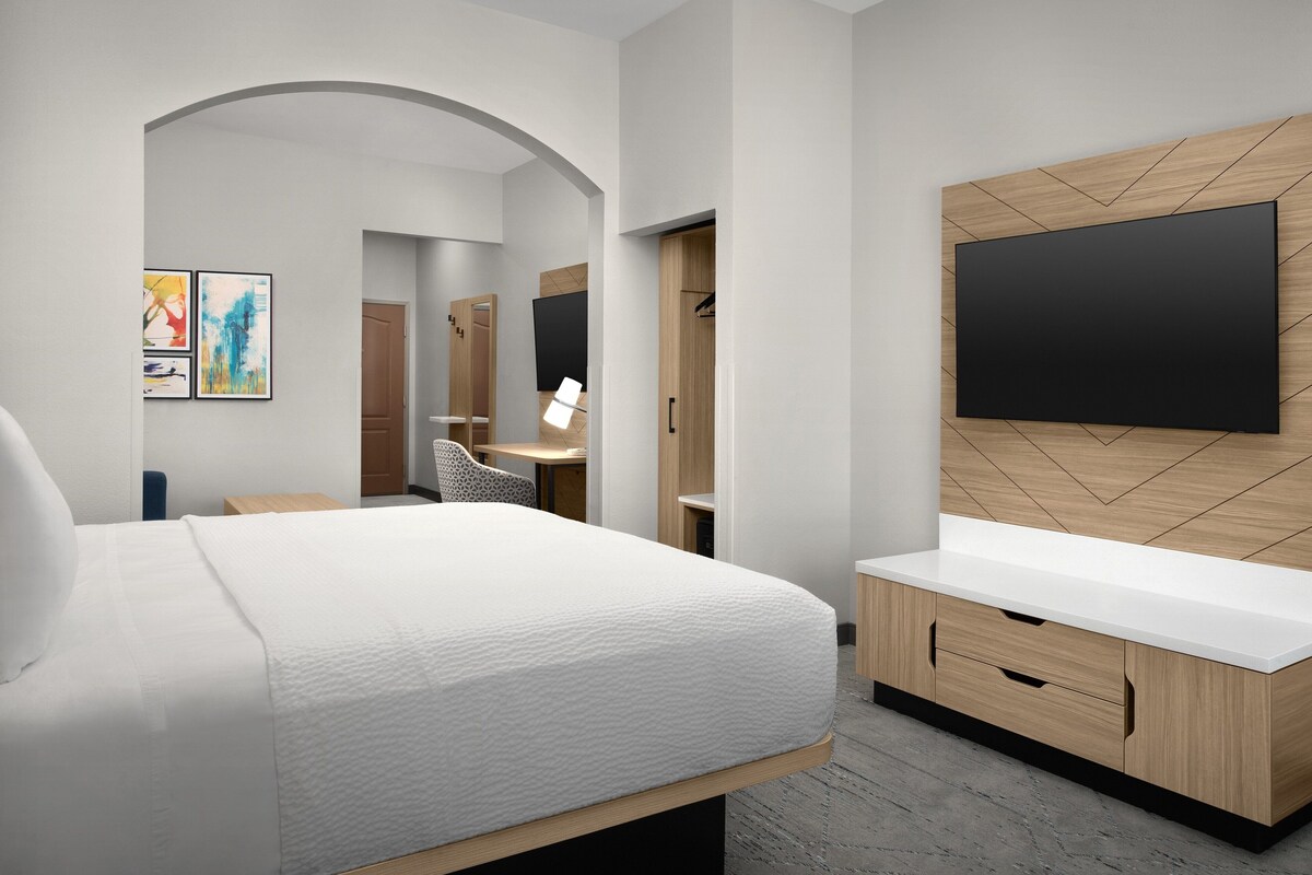 A modern hotel room with a bed, a TV mounted on a wooden wall, a desk, and a wardrobe.