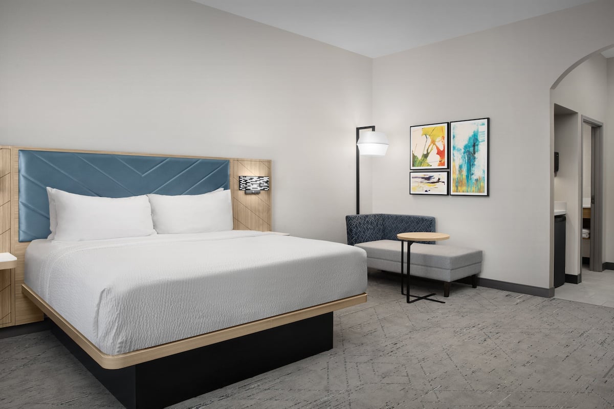 Una habitación de hotel moderna con una cama grande, un pequeño rincón de descanso y obras de arte en la pared.