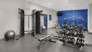 Un gimnasio con equipo de ejercicio, una banca y mancuernas.