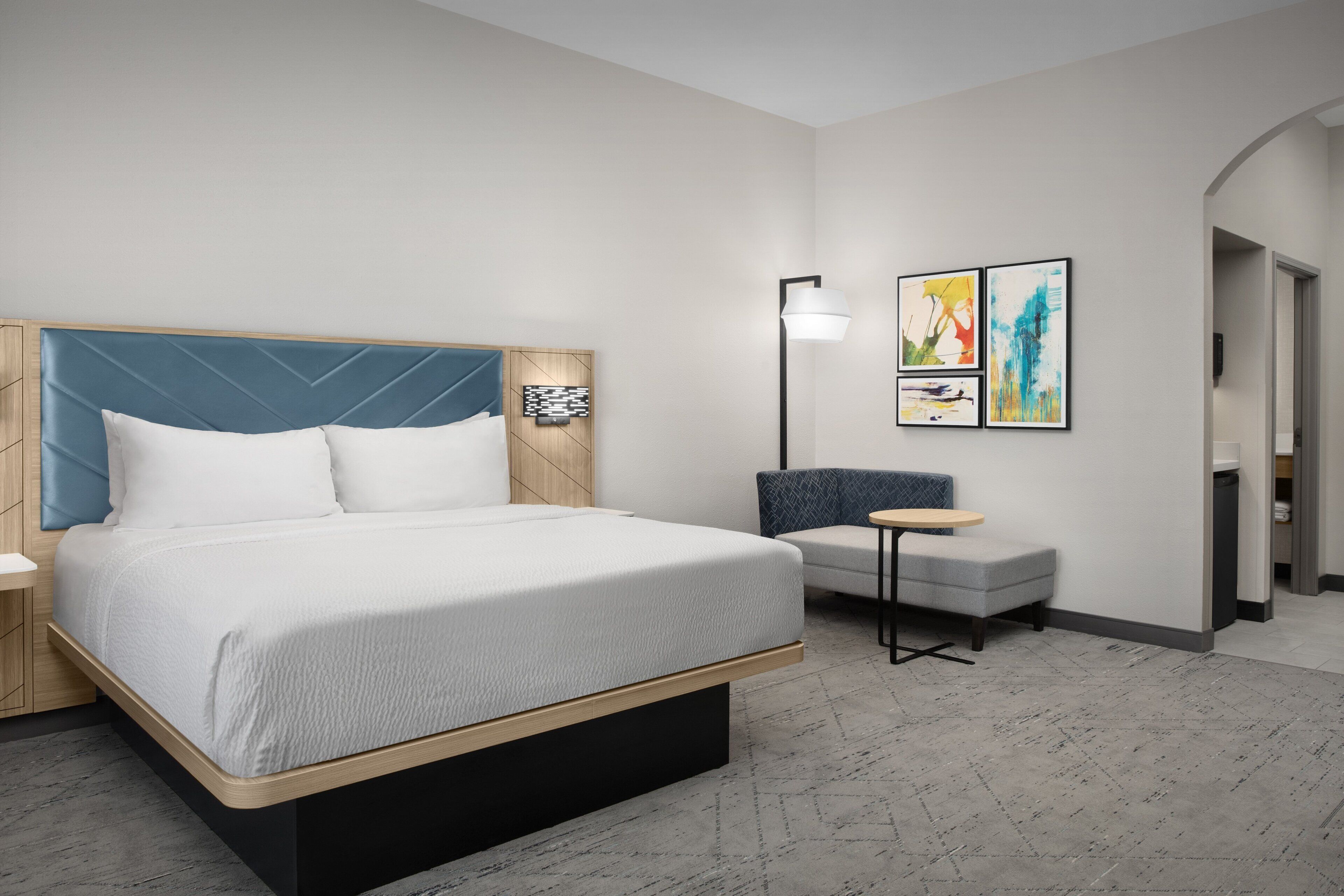 A modern hotel room with a large bed, a small seating area, and artwork on the wall.