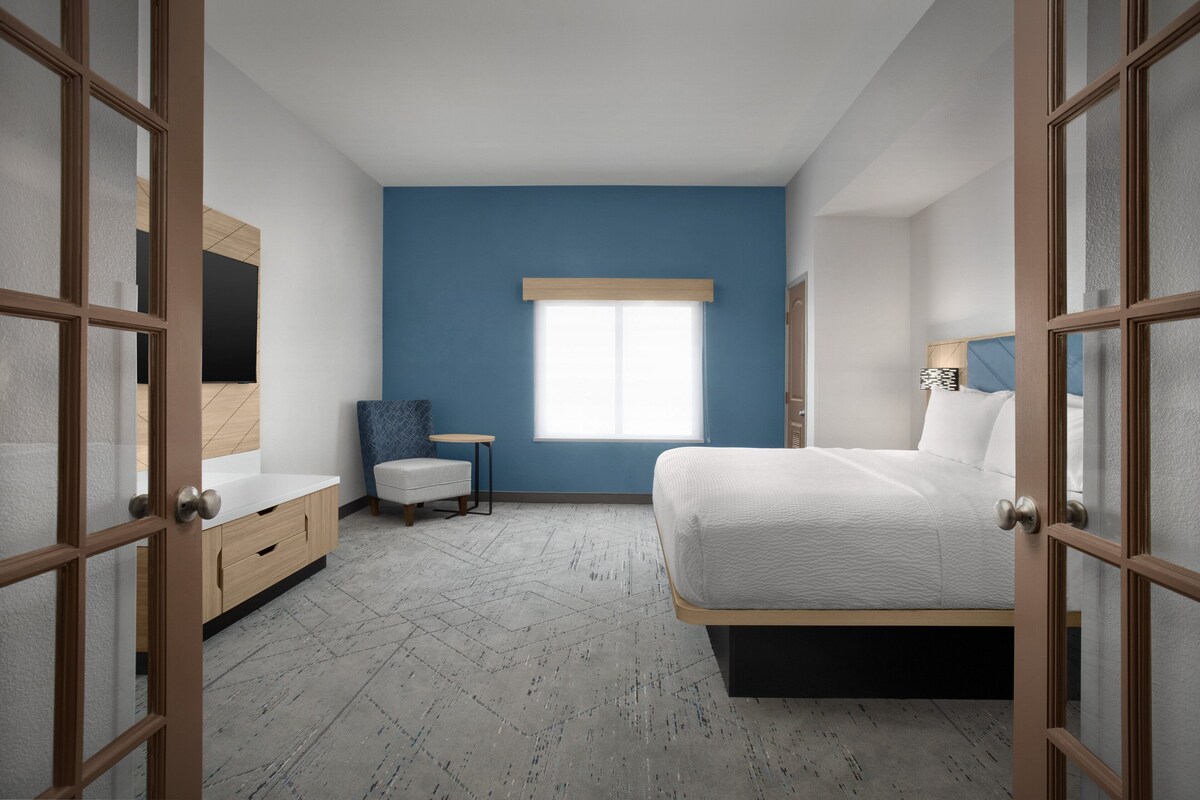 A bedroom with a bed, a chair, a small table, and a window.