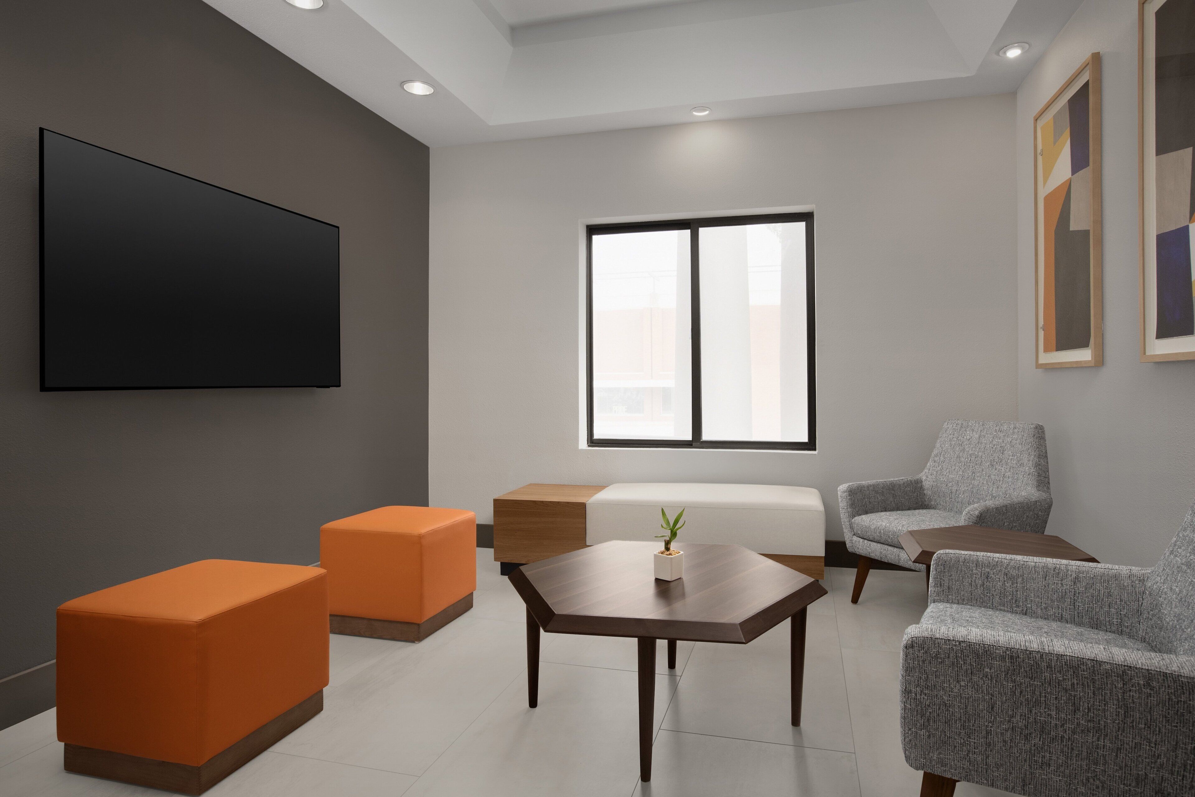 Una sala de estar moderna con un televisor de pantalla plana, sofás naranja y grises, una mesa de centro de madera y un ventanal grande.