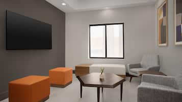 Una sala de estar moderna con un televisor de pantalla plana, sofás naranja y grises, una mesa de centro de madera y un ventanal grande.