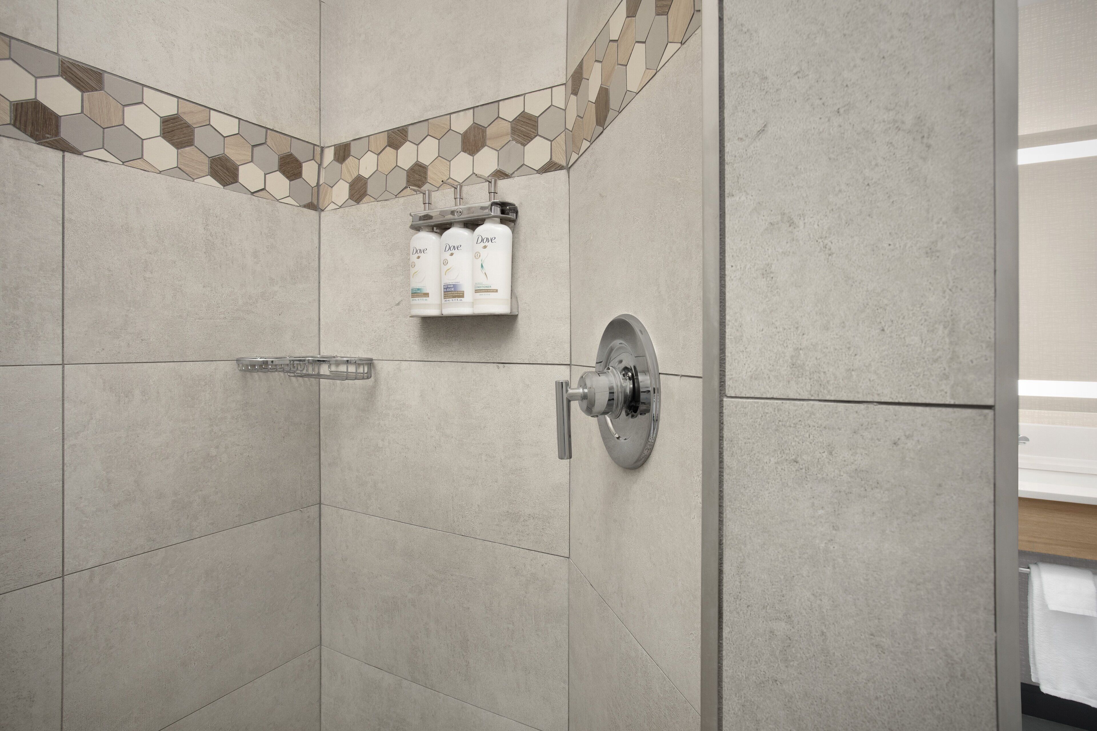 Un espacio de ducha con patrones de azulejos hexagonales, un dispensador de jabón en la pared y un secador de manos.