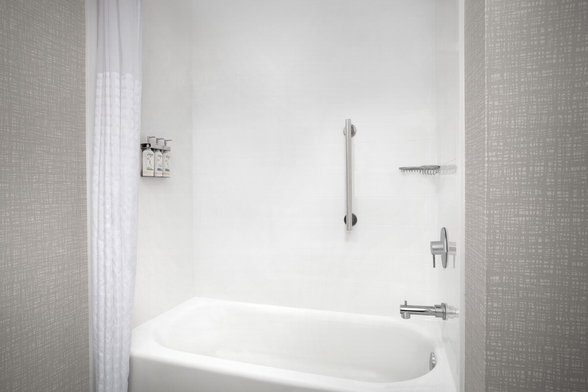 A modern bathroom with a white bathtub, a handheld showerhead, and a wall-mounted faucet.