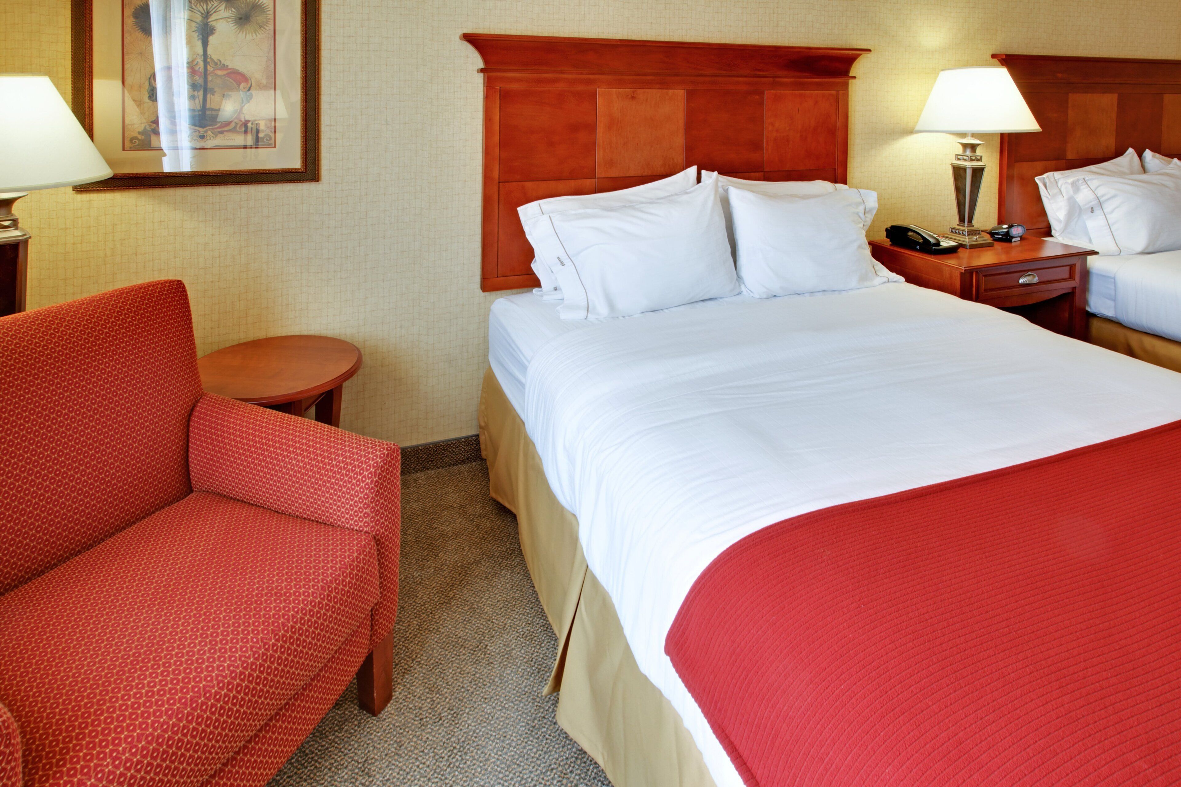 Una habitación de hotel con cama, una silla, una mesita de noche y una lámpara.