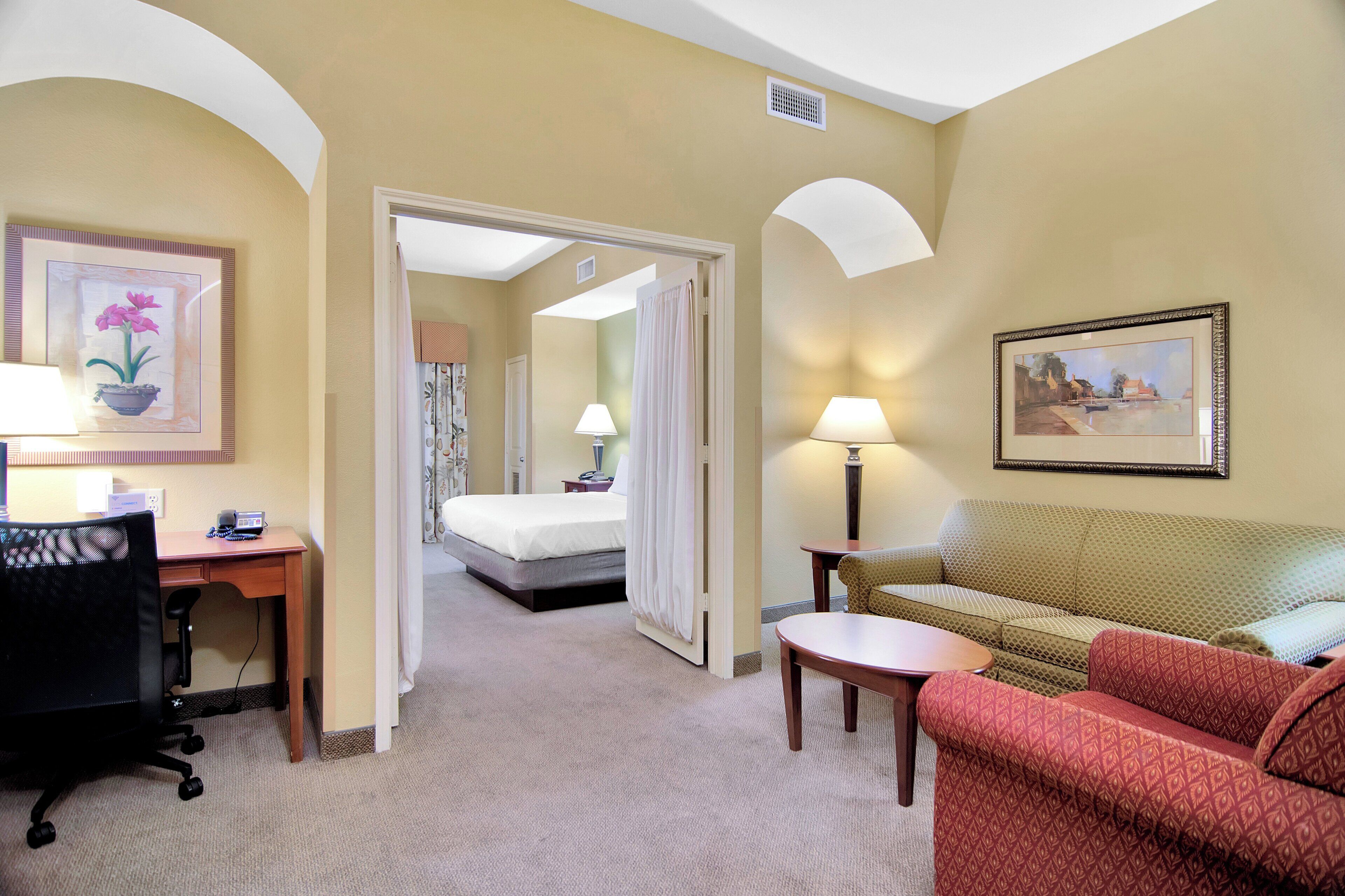 A hotel room with a bed, a desk with a chair, a sofa, and two lamps.