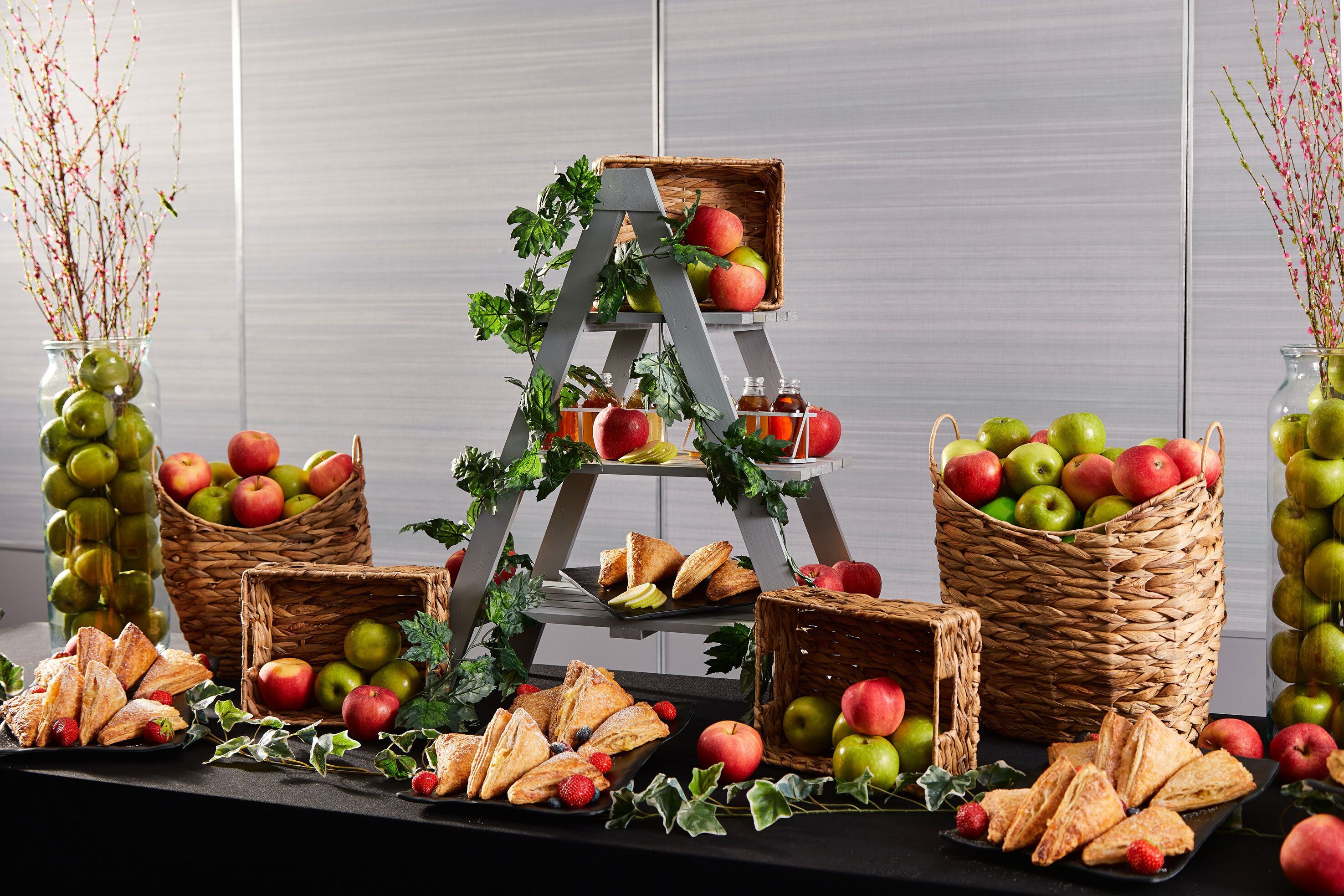 A table with baskets of apples, pastries, and a tiered stand with apples and honey bottles.