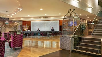 A hotel reception area with a reception desk, a large wall of inspirational quotes, and a staircase with a metal railing.