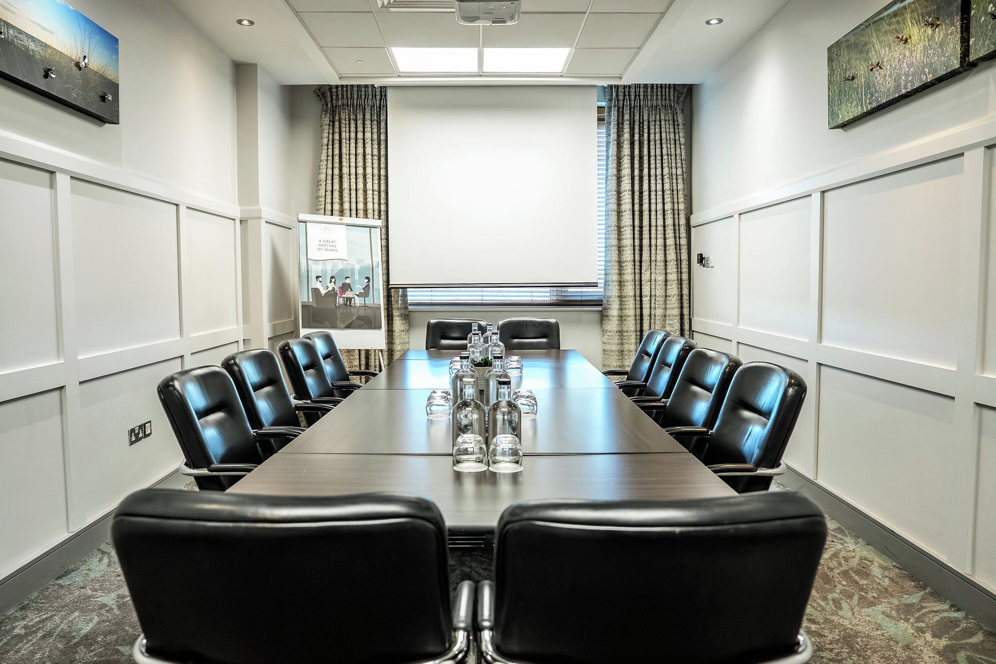 A conference room with a long table, black leather chairs, and a projector screen.