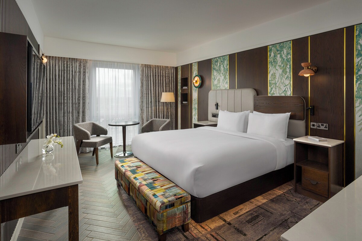 Una habitación de hotel moderna con una cama grande, un escritorio pequeño, una silla y un banco.
