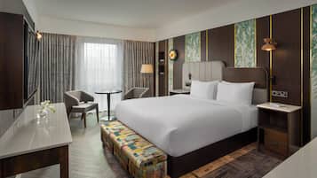 Una habitación de hotel con una cama grande, un escritorio, una silla, una mesita y un banco.