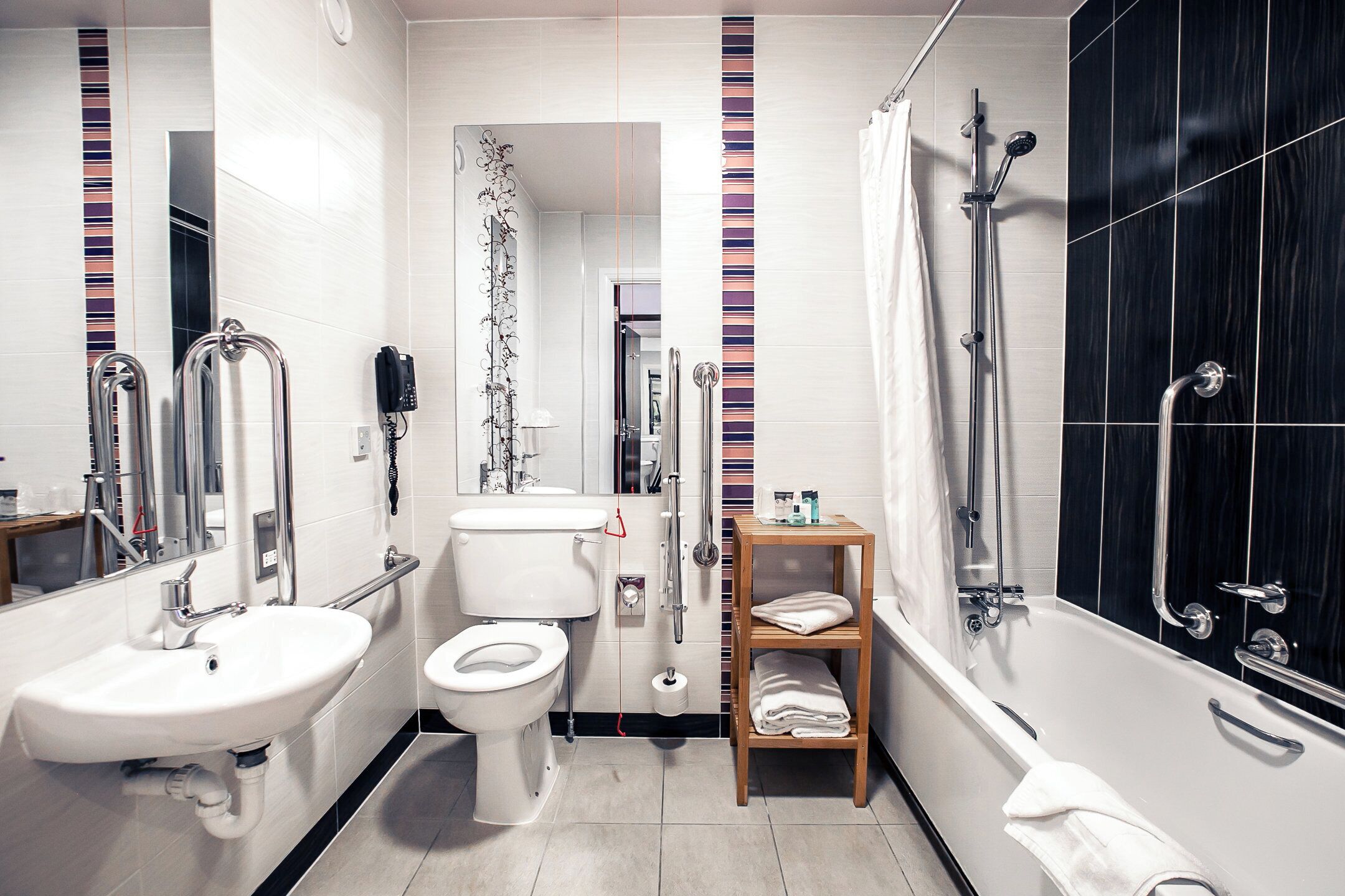 Un baño moderno con inodoro, lavabo, ducha y un estante de madera con toallas.