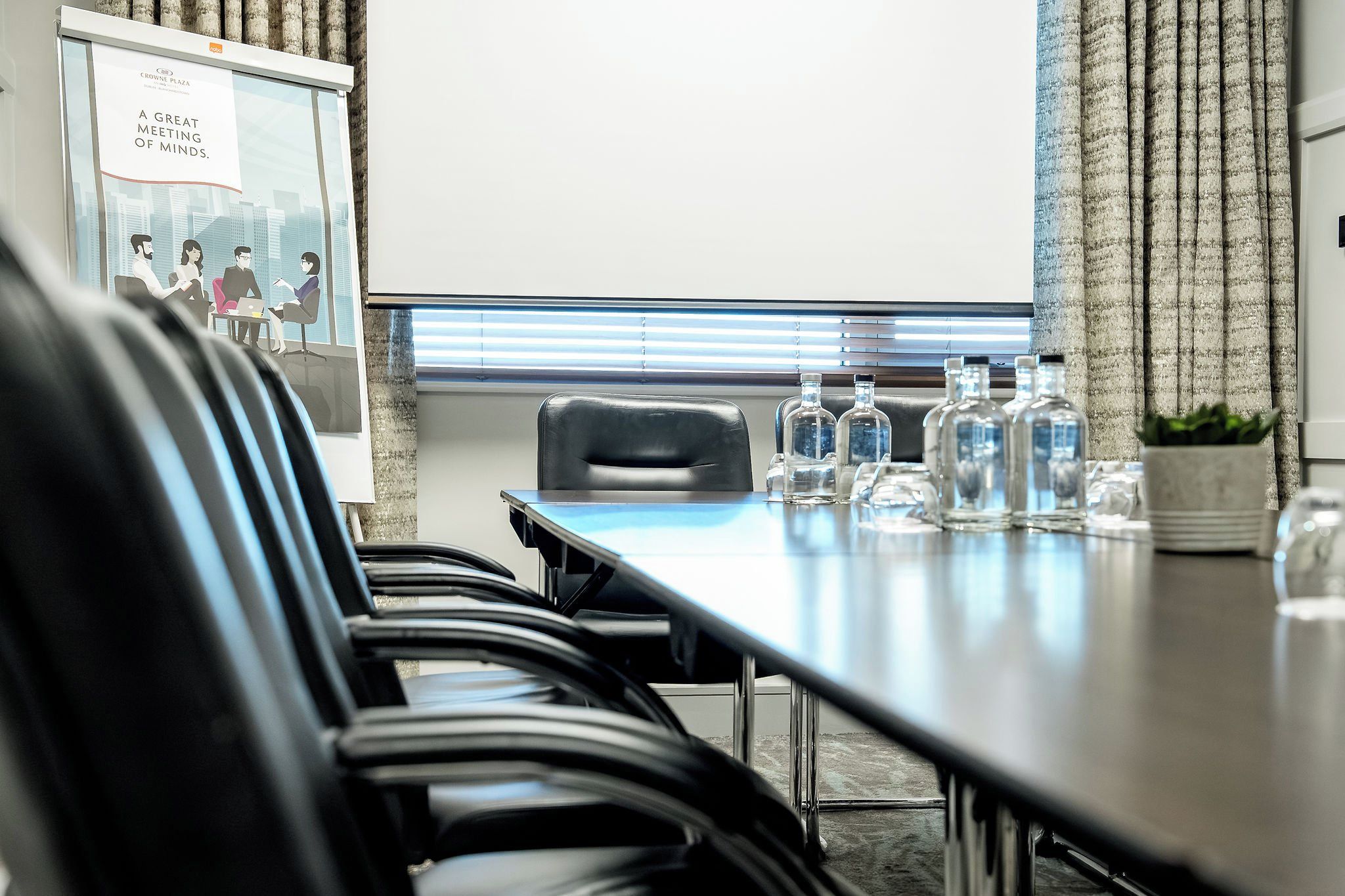 A conference room with a long table, chairs, and a projector screen.