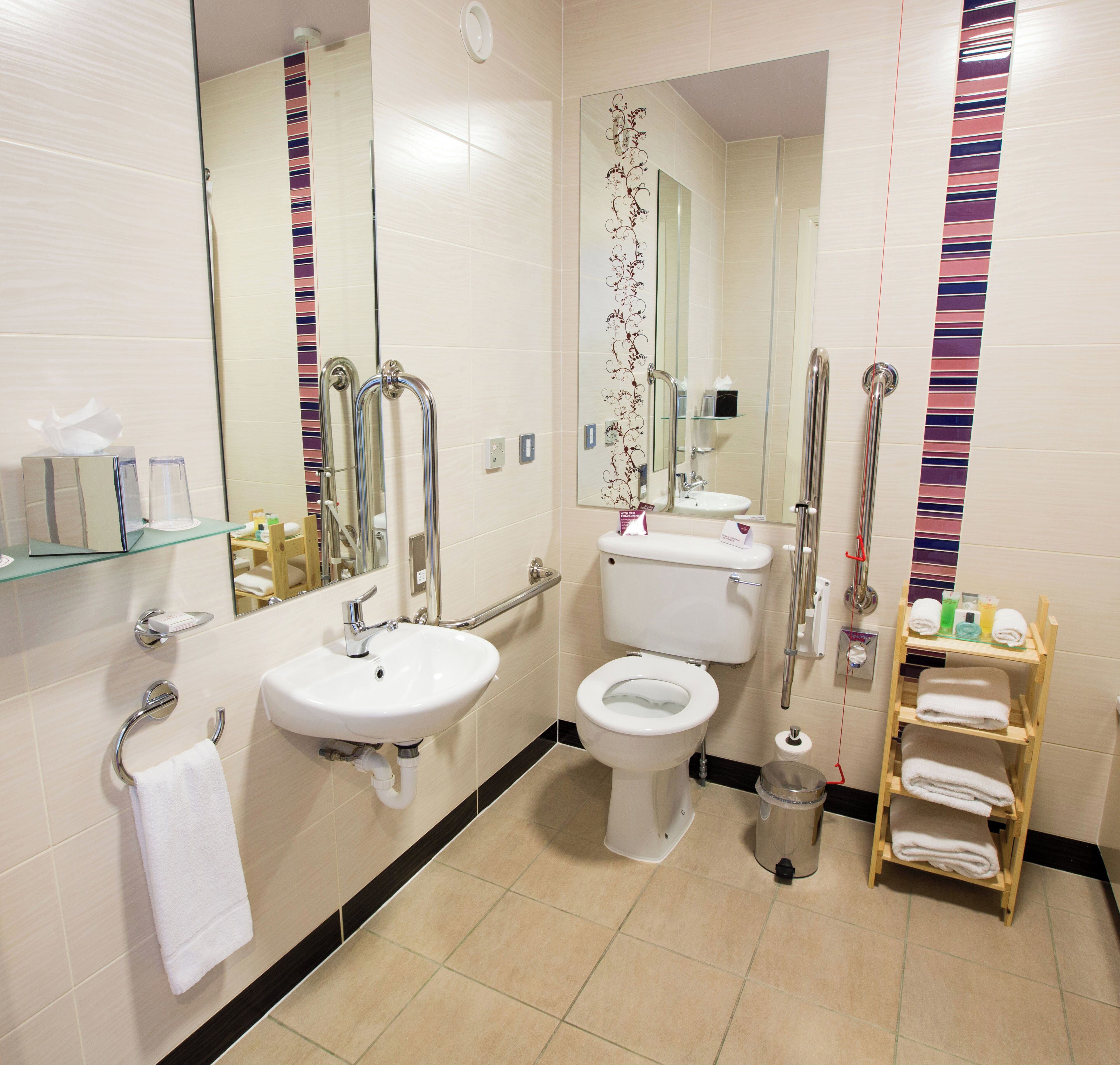 Un baño moderno con inodoro, lavabo y barras de apoyo.