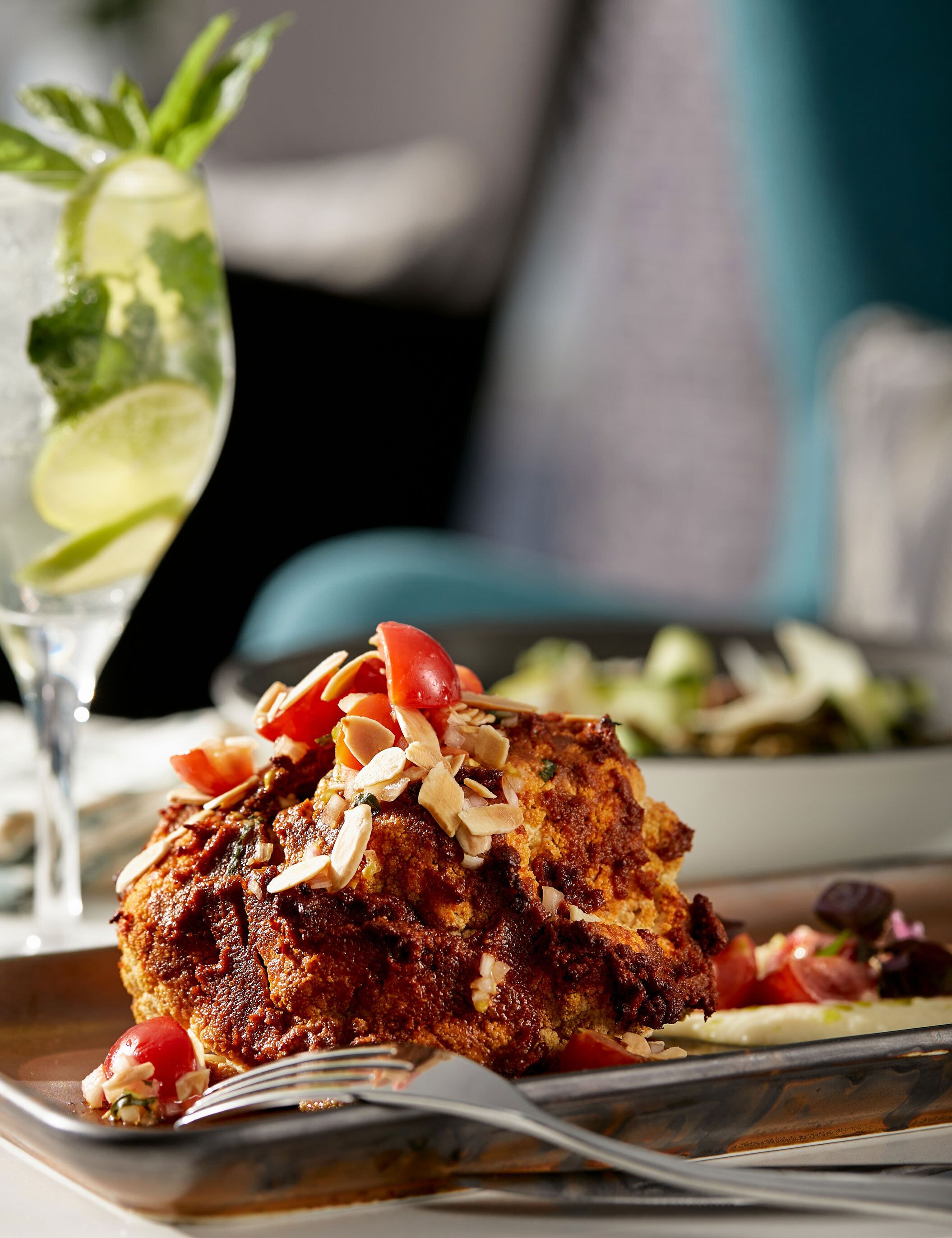 A meal with a piece of food topped with almonds and a drink with a lime garnish.