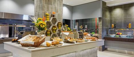 A buffet area with various breads, pastries, and a decorative arrangement of sunflowers and flowers.