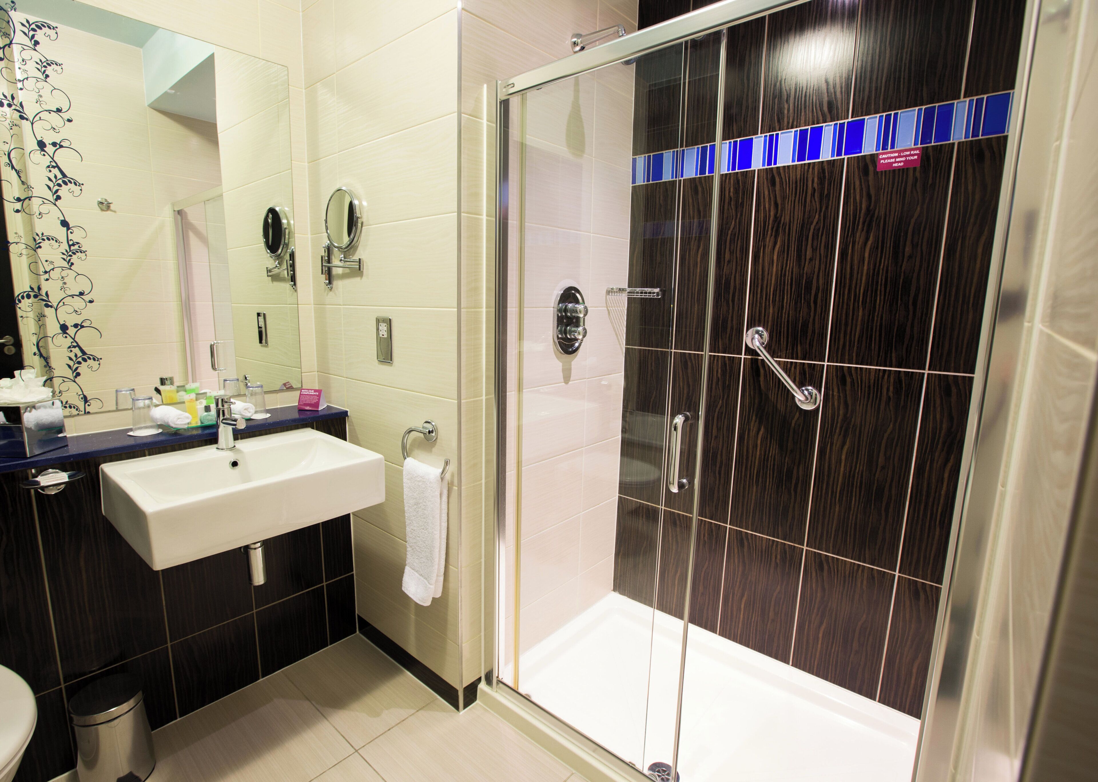 A modern bathroom with a glass-enclosed shower, a sink with a mirror, and a towel rack.