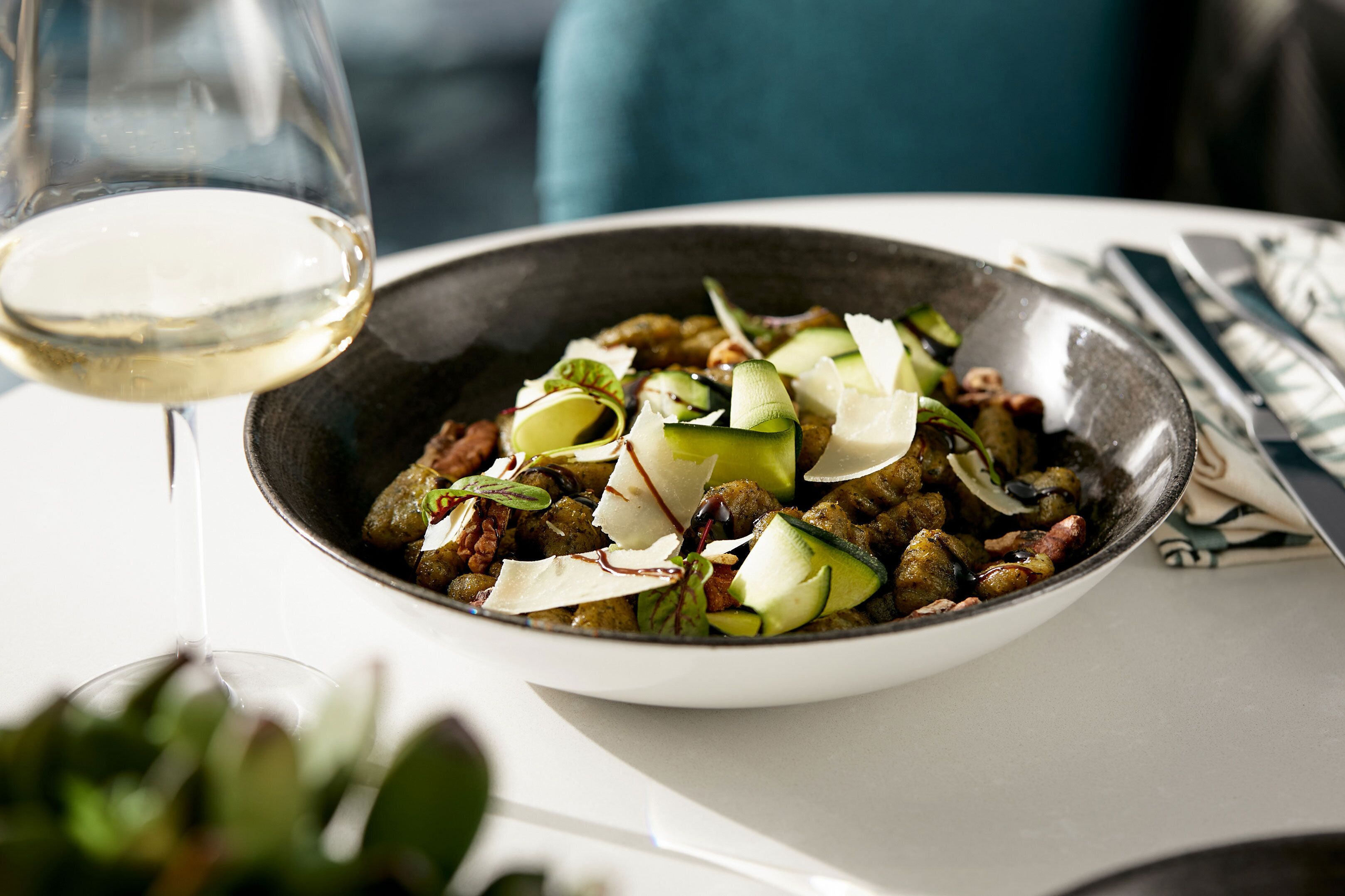 A bowl of food with a glass of white wine on a table.