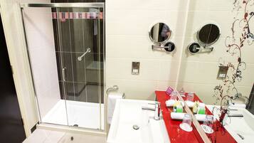A bathroom with a glass-enclosed shower, a sink with a red countertop, and two wall-mounted mirrors.
