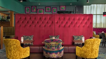 A seating area with a tufted red headboard, two yellow chairs, and a table with a candle.