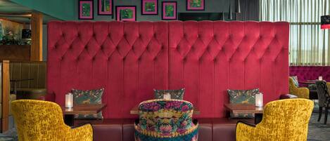 Zona de estar con cabecera tapizada roja, dos sillas amarillas y una mesa con una vela.