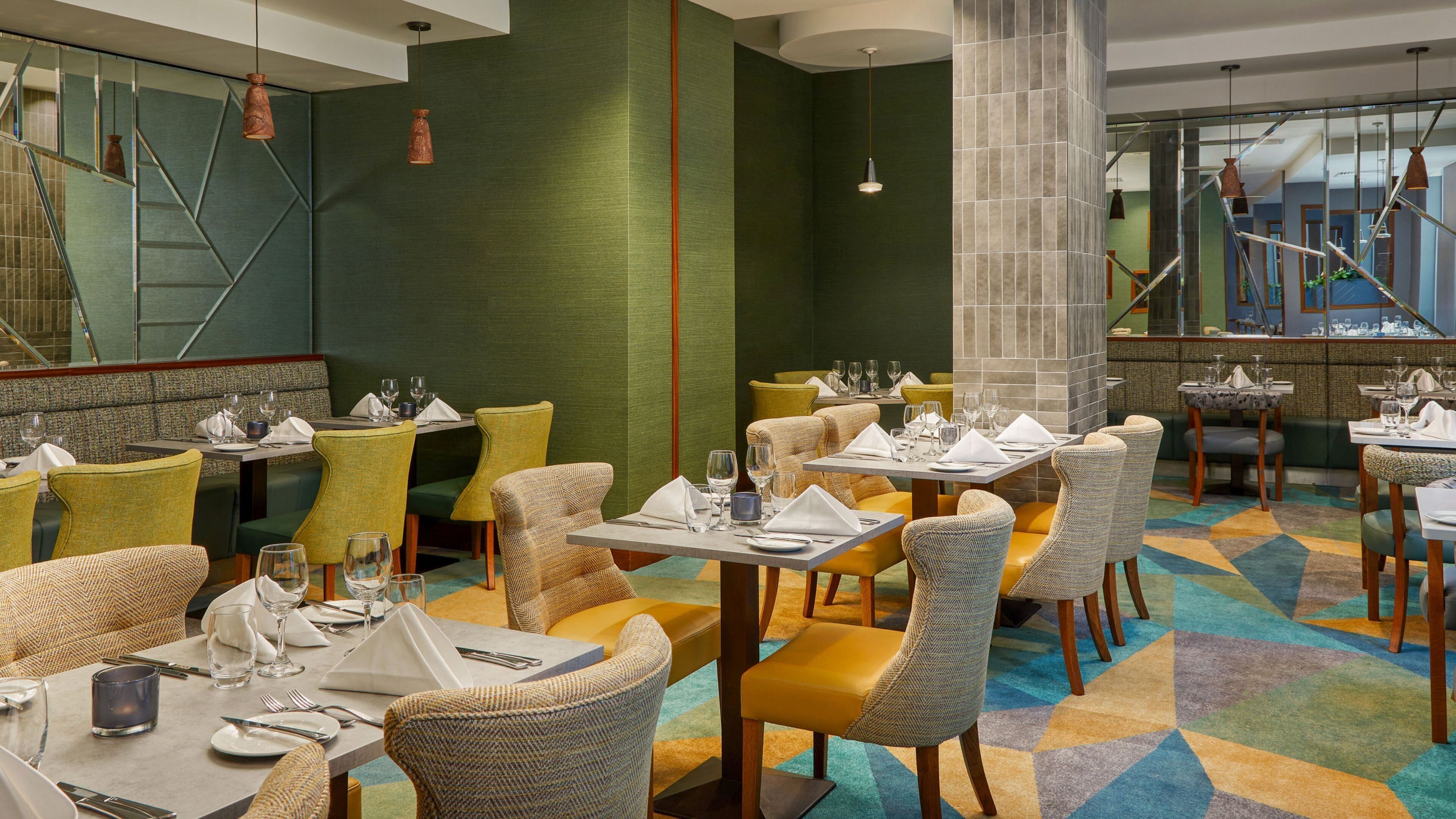Un restaurante con varias mesas y sillas, una alfombra estampada y una pared verde.