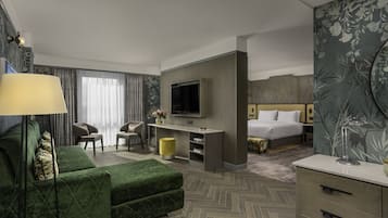 Una habitación de hotel con sofá verde, televisión, cama, escritorio y silla.
