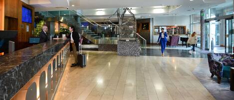 A modern hotel lobby with a reception desk, a staircase, and a seating area.