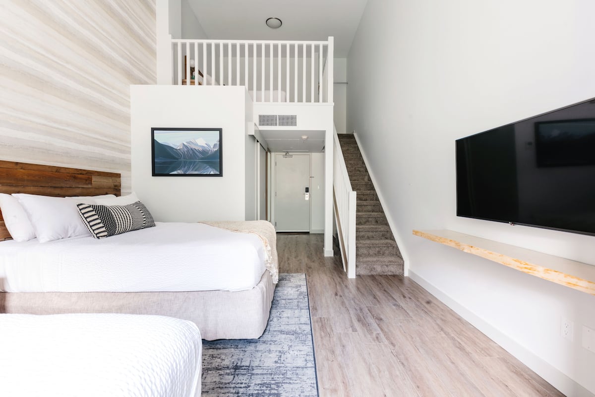 Un dormitorio moderno con una cama grande, un televisor montado en la pared y una escalera que lleva a un nivel superior.