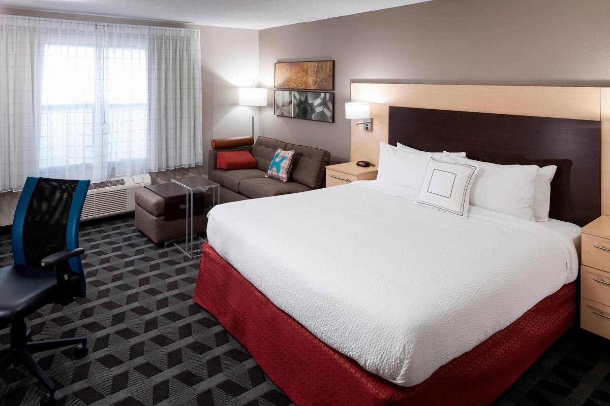 A hotel room with a large bed, a desk, a chair, a sofa, and a window with curtains.