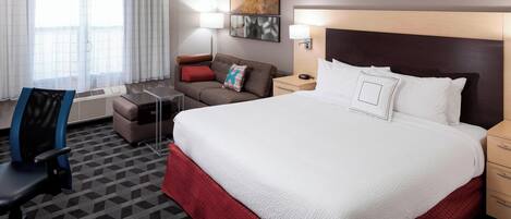 A hotel room with a large bed, a desk, a chair, a sofa, and a window with curtains.