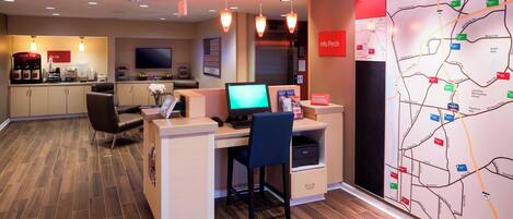 A hotel reception area with a computer desk, chairs, a coffee station, and a map on the wall.