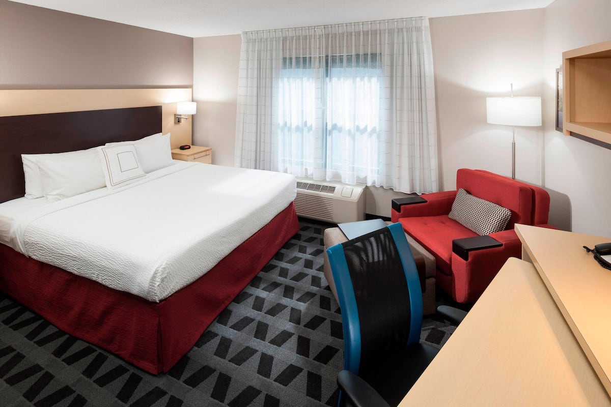 A hotel room with a large bed, a desk, a chair, a red sofa, and a window with curtains.